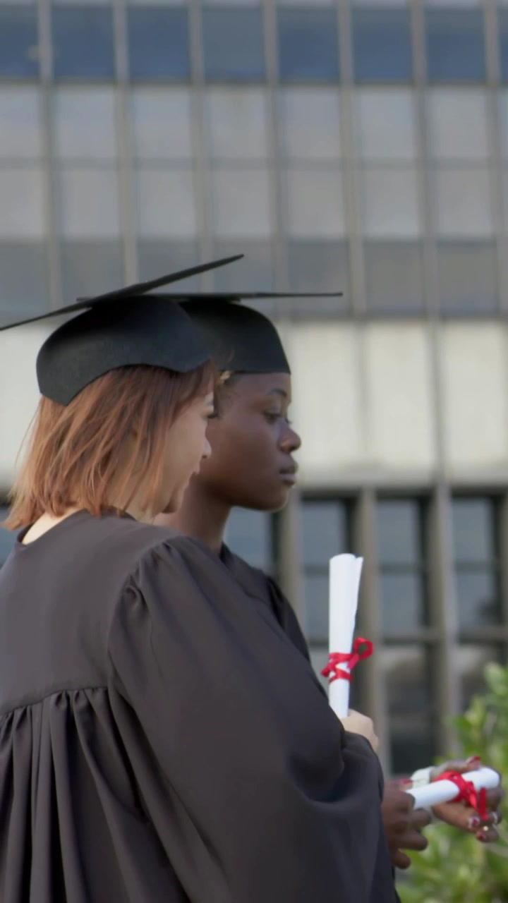 Vertical video: Hand offering diploma offscreen, grads holding diplomas in caps at graduation