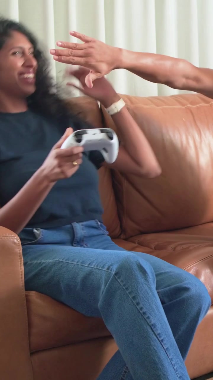 Vertical video: Reacting to game and man's reach, woman laughing, holding gamepad on tan sofa