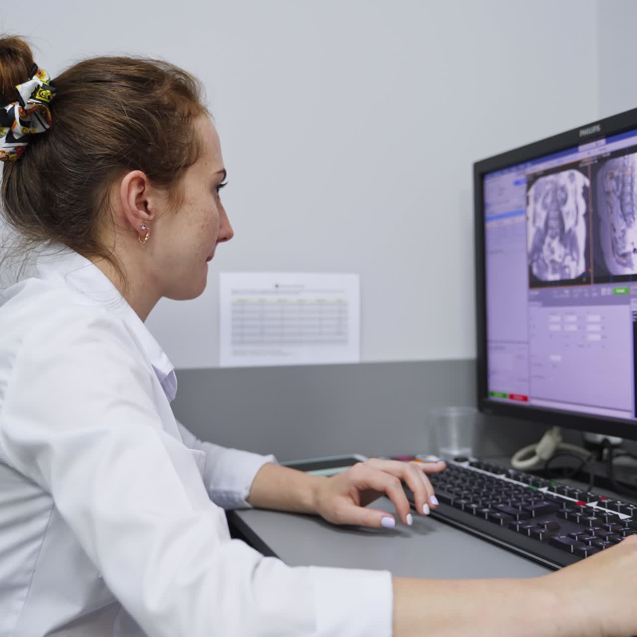 Young female medic at the computer analyzing the MRI scans. Lab technician working in modern clinics. Side view