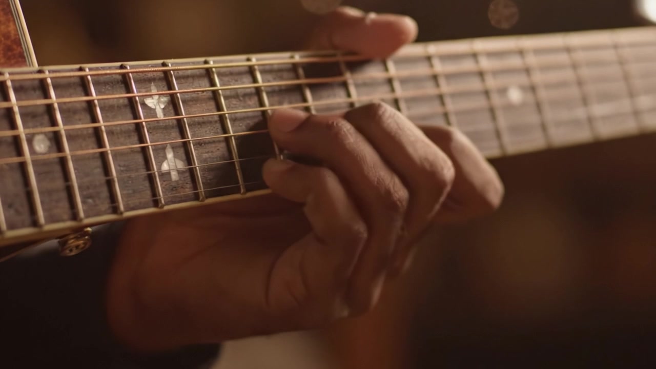 Primo piano suggestivo di una mano che suona abilmente le corde della chitarra, mettendo in risalto l'arte e l'emozione della creazione musicale in un'atmosfera intima.
