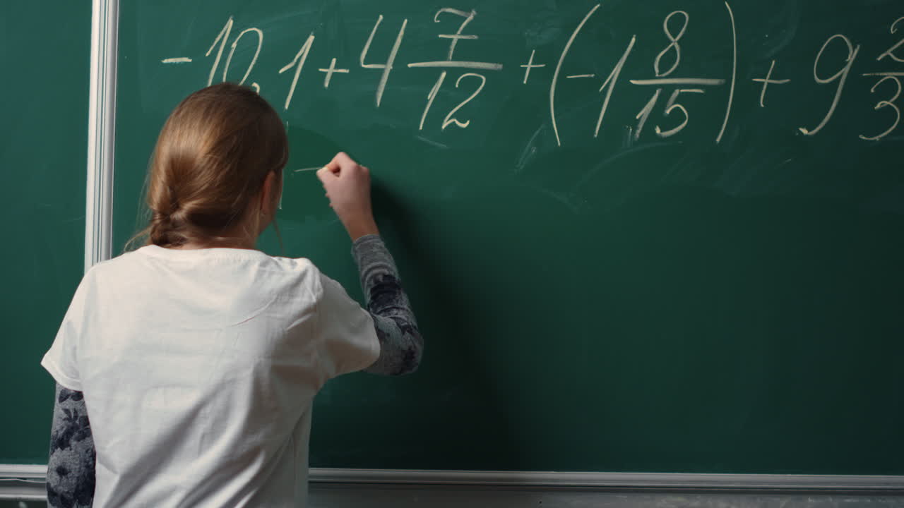 vista posterior de una escolar haciendo una tarea de matemáticas en la pizarra en la clase.estudiante escribiendo