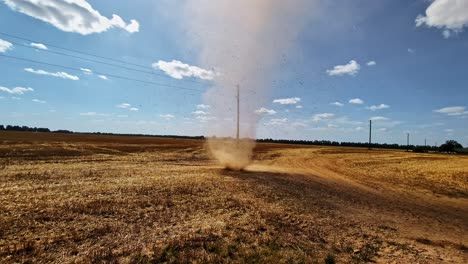 a sudden dust devil, small tornado, or whirlwind sand storm blows sand and debris into the sky above a field of freshly harvested crops during a drought