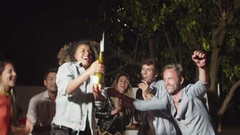 Happy-curly-haired-woman-popping-champagne-at-outdoor--party