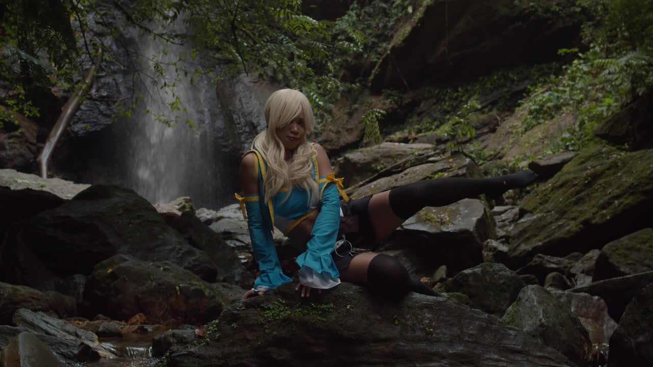 косплейщица люси сердцефилия сидит на скале и позирует у основания огромного водопада