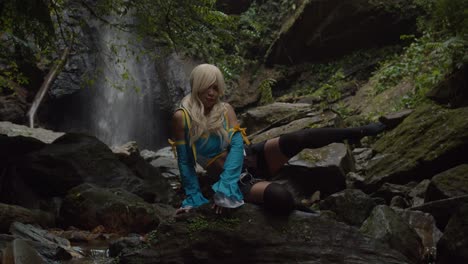 lucy heartfilia cosplayer sits on a rock striking a pose at the base of a huge waterfall