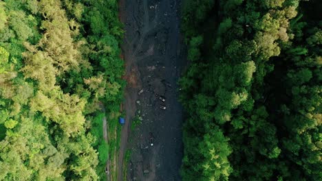 rocket drone footage of trucks at the bottom of a large dry river surrounded by trees