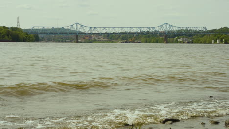 waves crashing the shore of the ohio river with rochester monaca bridge in the background on an overcast day