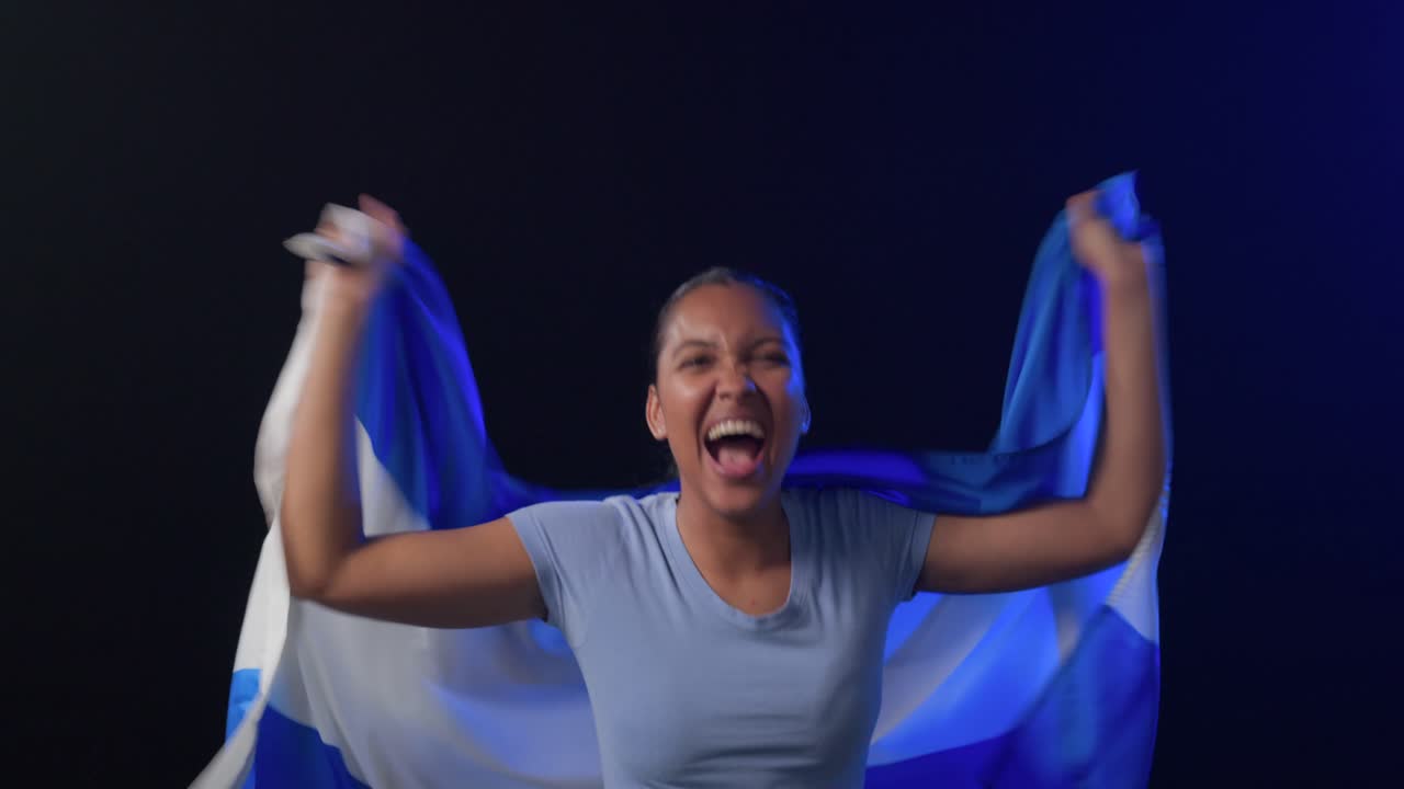 Flag being held up, African American woman stepping out, draping Argentina flag in studio, cheering