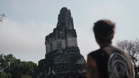 a man stands in reflection as he gazes at temple ii, the temple of the masks, in the heart of the great plaza at tikal, guatemala.