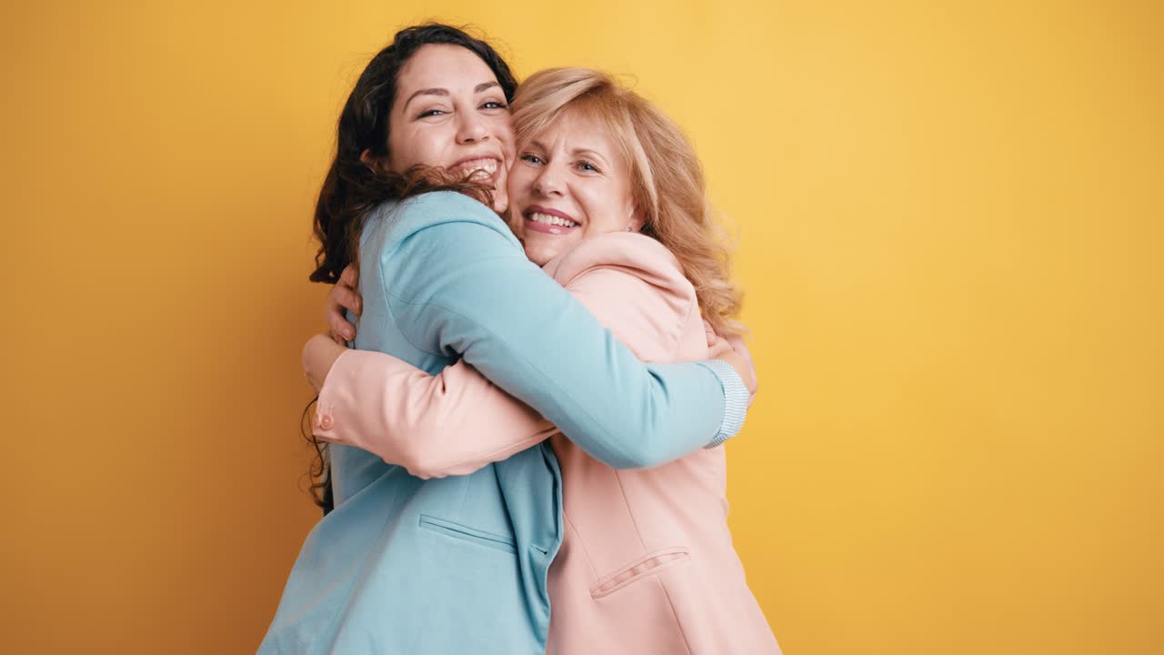 Due donne felici che si abbracciano e sorridono su sfondo giallo