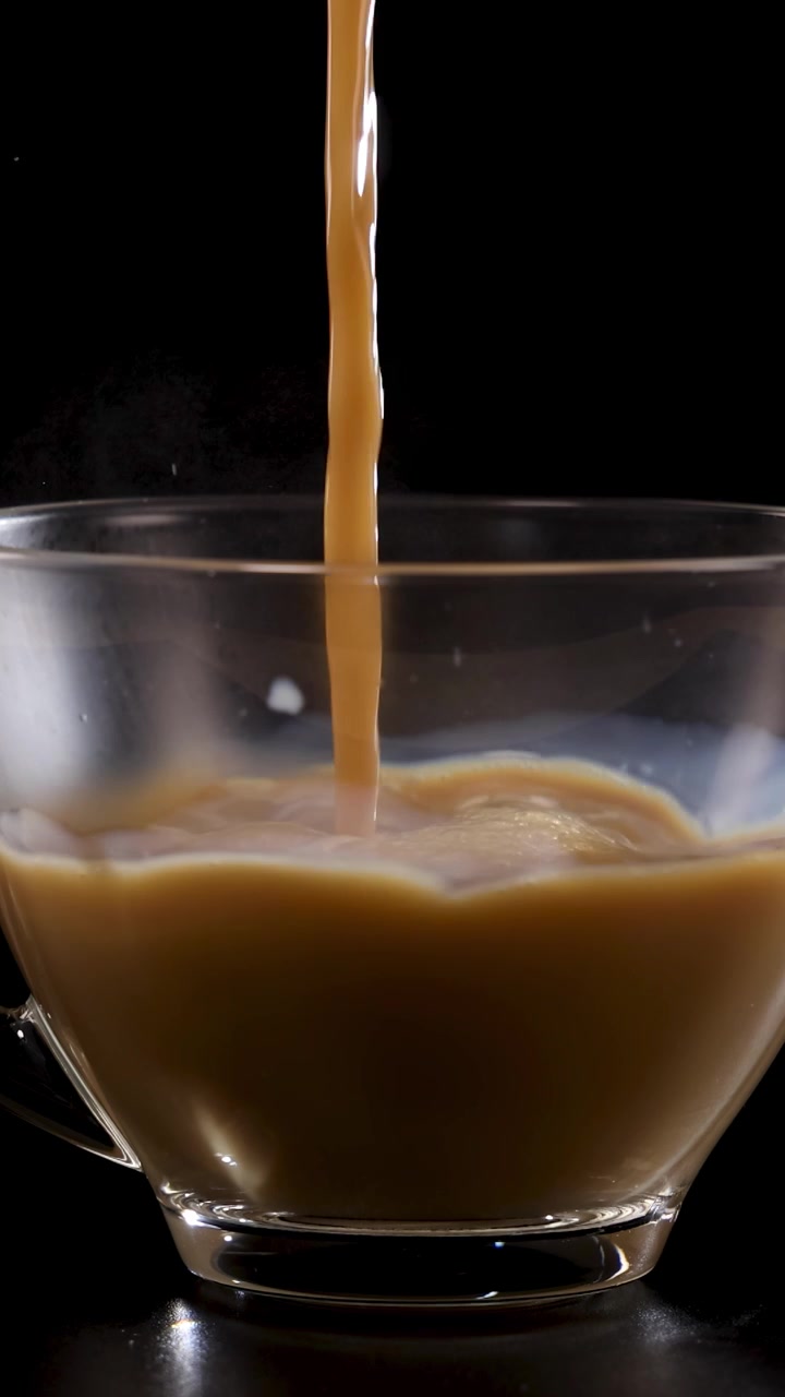 Il caffè viene versato in una tazza di vetro trasparente, creando un effetto vorticoso su uno sfondo scuro.