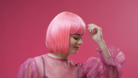 portrait of beautiful woman wearing a pink wig, dancing and laughing to camera on bright pink wall background