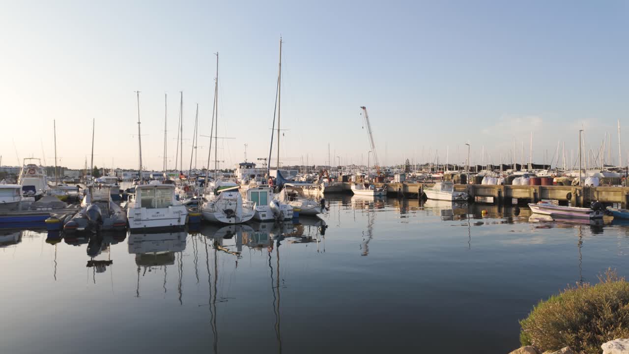 Daytime establishing pan of fishing boats docked in Lagos harbour, Portugal with blue sky and ocean