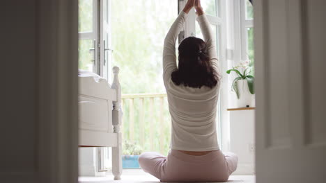 Vista-Trasera-De-Una-Mujer-Asiática-Madura-En-Pijama-Sentada-En-El-Suelo-Del-Dormitorio-Meditando-En-Pose-De-Yoga---Filmada-En-Cámara-Lenta