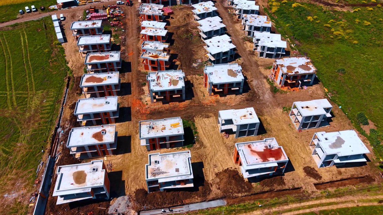 Vista diagonale dall'alto di un villaggio di cottage sul mare in costruzione. Ripresa con drone di strutture abitative in costruzione vicino a campi e alla costa.