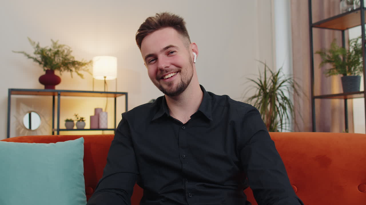 un tipo sentado en el sofá de casa, mirando a la cámara, haciendo una videoconferencia con amigos o familiares.