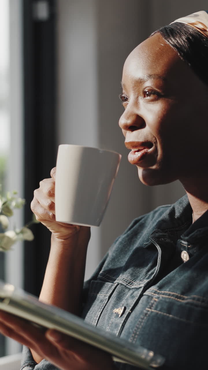 Glad ung, sort kvinde læser og drikker kaffe indendørs