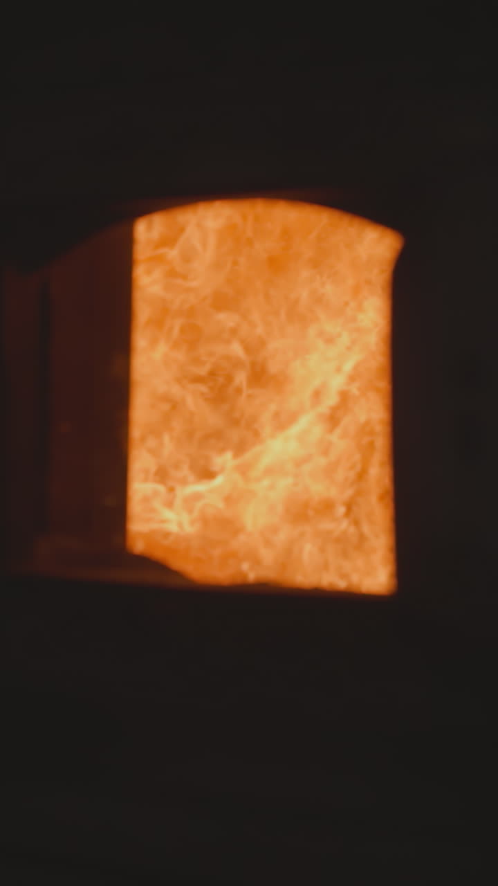Large flame burns in industrial furnace chamber with open door in dark factory workshop. Direct heater operates equipment at metalworking complex