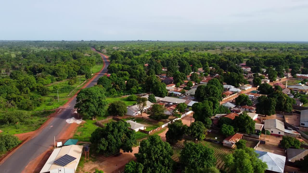 Inquadratura con carrello e panoramica a destra di un villaggio rurale africano boscoso con strada asfaltata accanto alla costa in Gambia