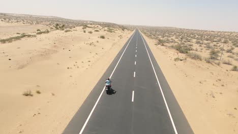 Aerial drone shot following a motorbike leaving a trail of dust on a lonely desert highway.