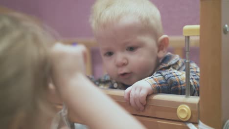 little baby leans on cot playing with elder sister in room