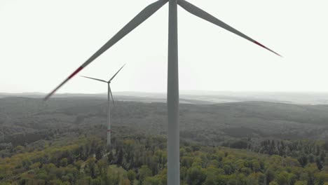 Aerial-dolly-shot-of-wind-turbines-one-in-foreground-and-another-in-full-shot,-bright-daylight