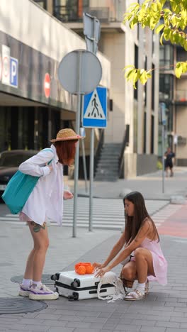 two women helping each other with luggage on the street