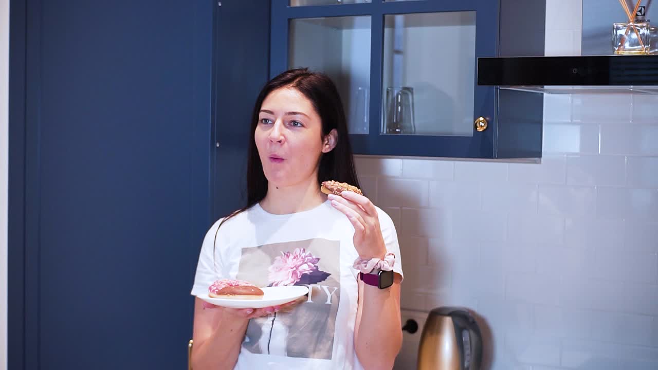 una joven sostiene el plato con donuts y come un donut de chocolate en la cocina, disfruta de su dulce desierto
