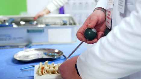 long metal spike tool with a ball handle in the hand of an unrecognized male wearing white robe. educator neurosurgeon demonstrates the usage of instrument at spine model. close up.