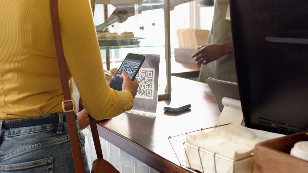 Young African American man scans a QR code from a biracial woman's phone at a cafe