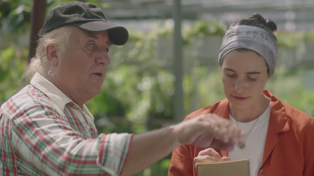 Nurseryman Working with Female Colleague in Greenhouse