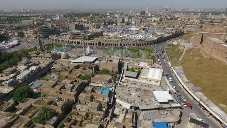 an aerial shot of the city of erbil showing the ancient erbil citadel and the garden opposite the castle with water fountains and the popular market