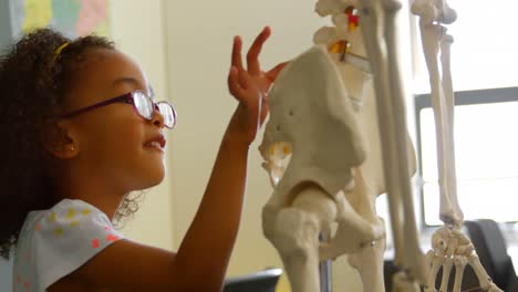 vista lateral de una colegiala afroamericana aprendiendo el esqueleto humano en el aula de la escuela 4k