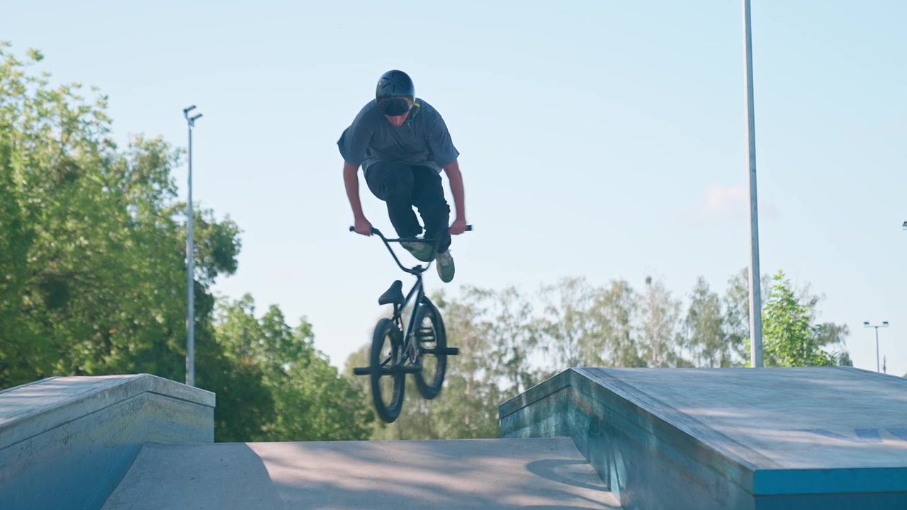 Ung mand på BMX-cykel udfører et springtrick i en skatepark