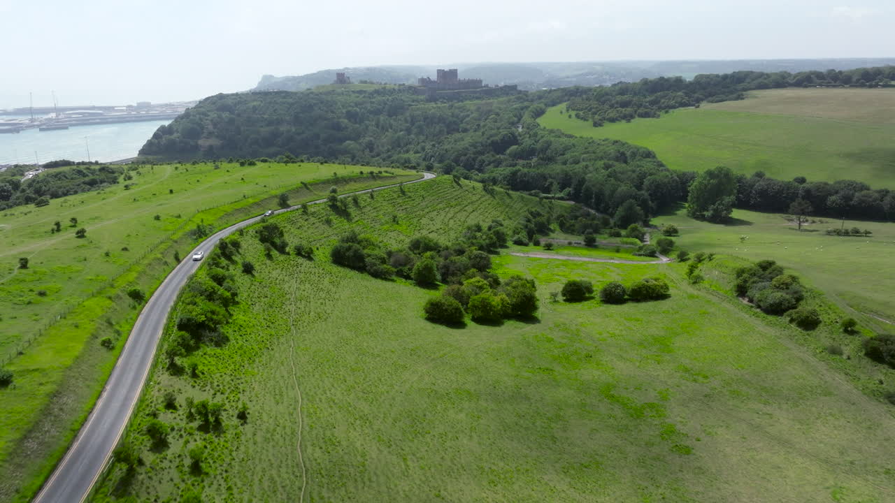 Winding Road Through Lush Green Hills With Dover Castle Revealed In Distance. Kent, England. aerial tilt-up shot