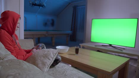 young man watching tv and using mobile phone, sitting on the couch at home in the evening, chroma key