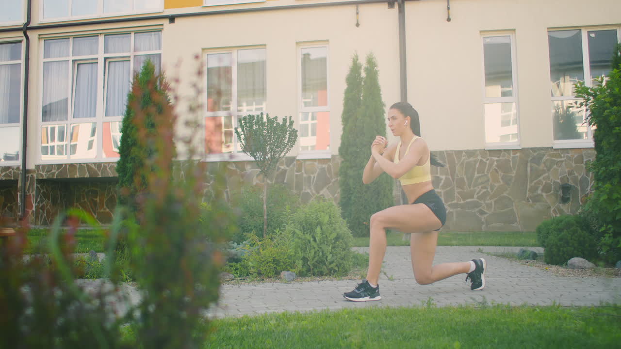 entrenamiento de las piernas y las caderas en el parque de la ciudad. mujer joven hace estocadas en el parque de la ciudad en la pasarela