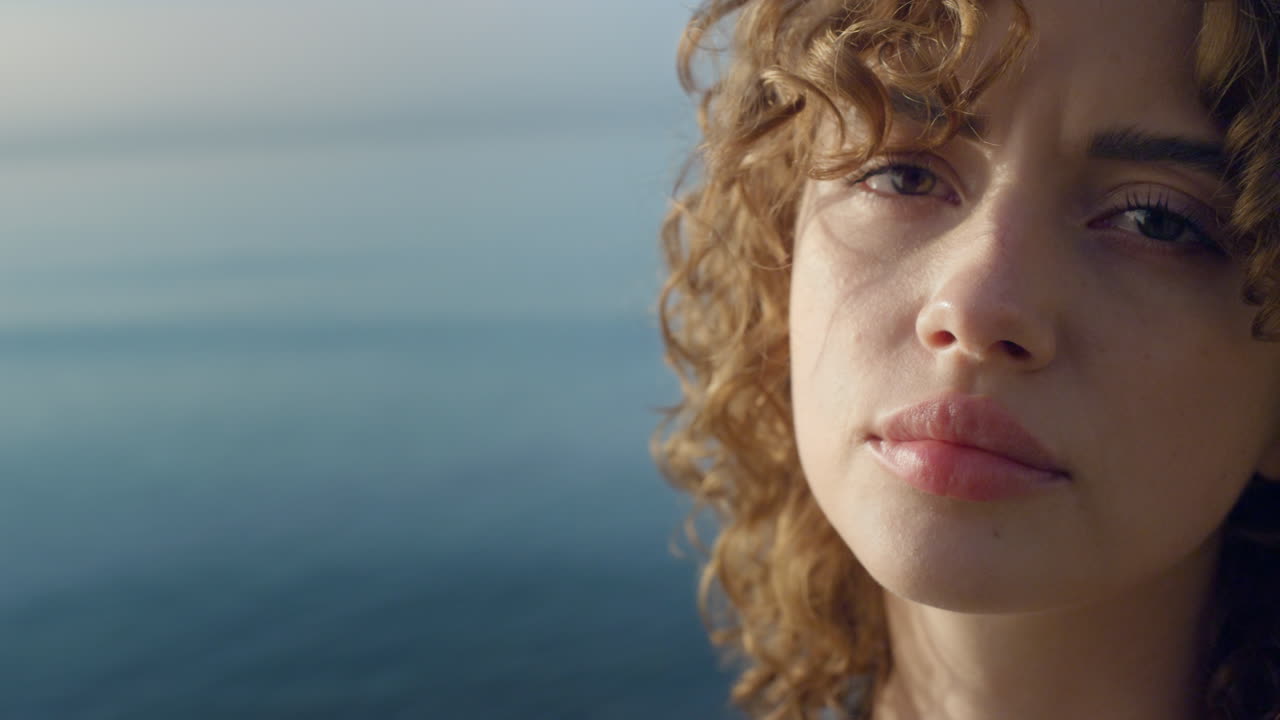 Donna scontenta in posa davanti alla fotocamera al mare. Ragazza allegra con espressione seria.