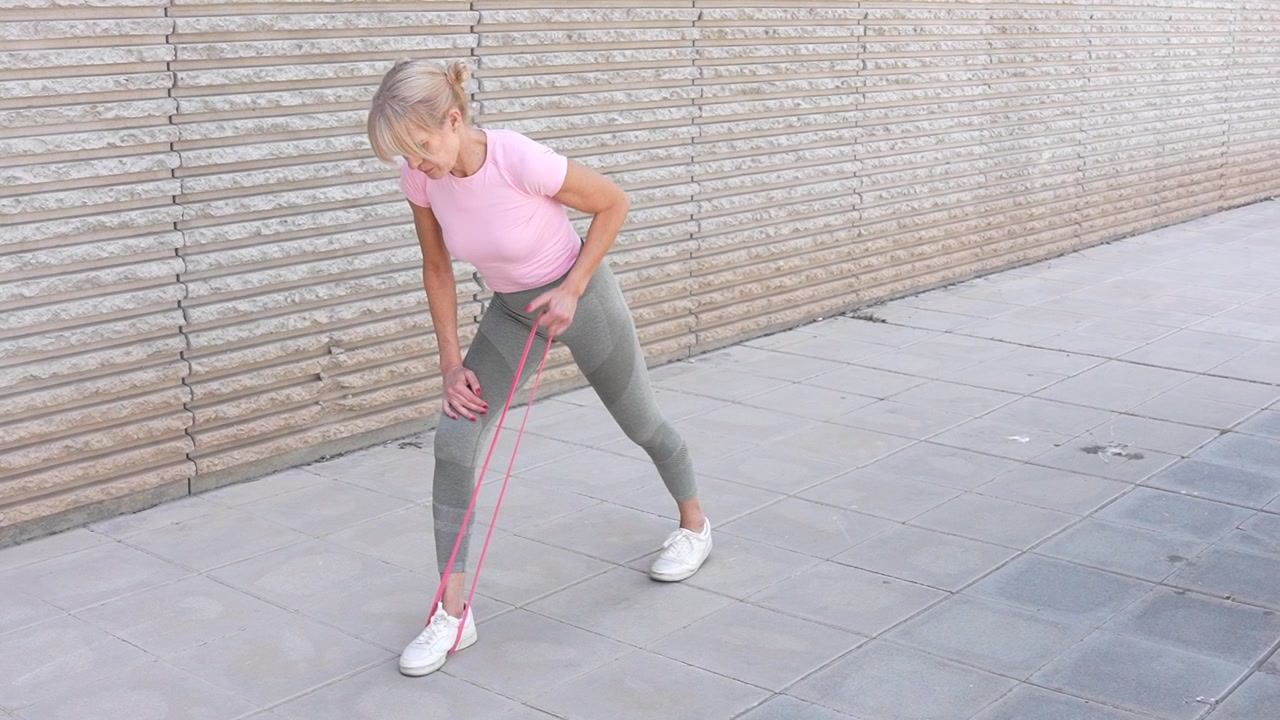 Woman exercising with resistance band outdoor in sportswear focus on fitness and health