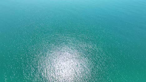 reverse aerial dolly over open ocean with sunlight reflection glistens