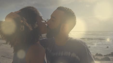 animation of lens flares over diverse couple embracing and kissing on beach against sea and sky