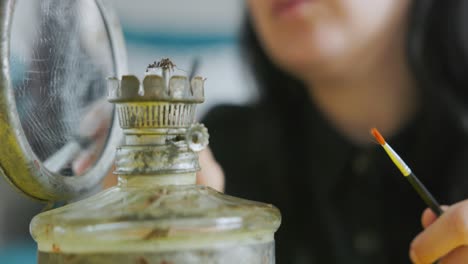 un primer plano de una mujer que limpia el polvo con una lámpara de gas vintage.