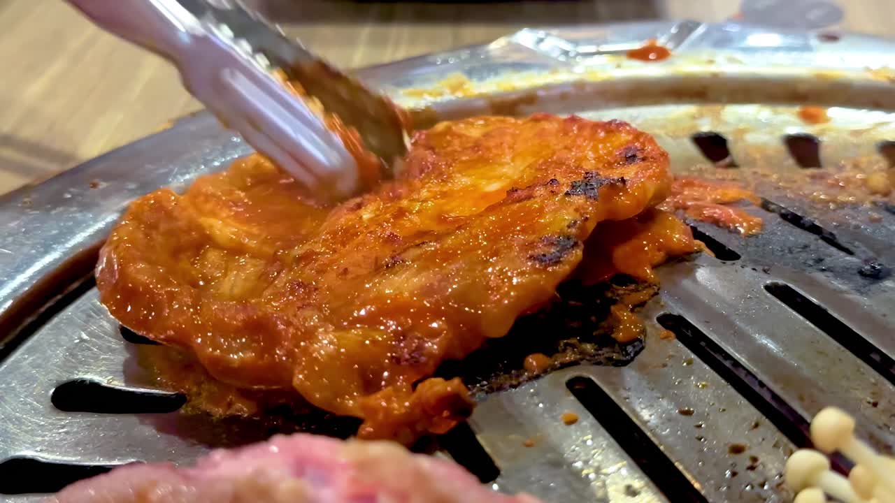 Grilled meat and mushrooms sizzle on a Korean BBQ grill in a vibrant Bangkok setting, showcasing culinary techniques and flavors