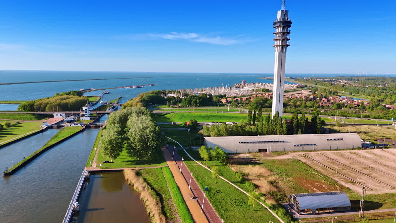 Beautiful shore of Lake Markermeer on clear sunny day. Drone footage along the lakefront approaching the telecom tower and yacht club.