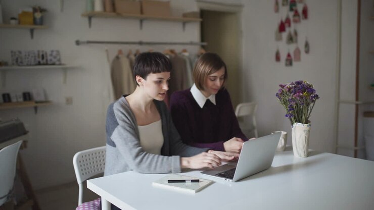 Due giovani donne sedute al tavolo usano il notebook. Una donna lavora al computer portatile.