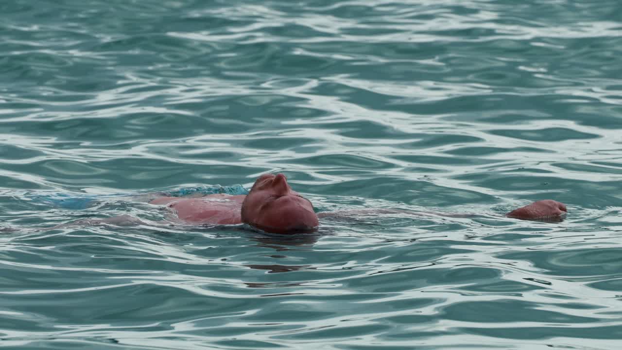 A man peacefully floats on his back in the ocean near Phuket, Thailand, under natural daylight with gentle camera movement