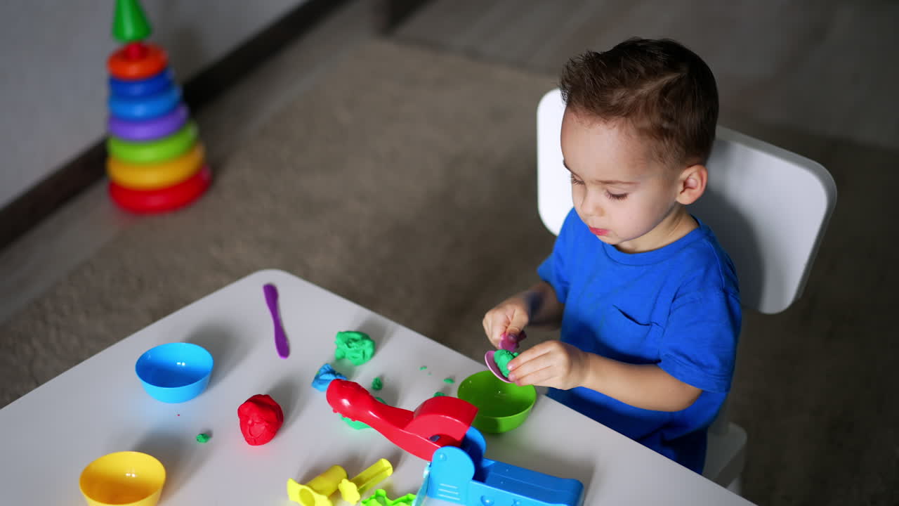 Lovely child holding a plastic spoon and a piece of plasticine. Focused baby boy doing art hobby. Top view.