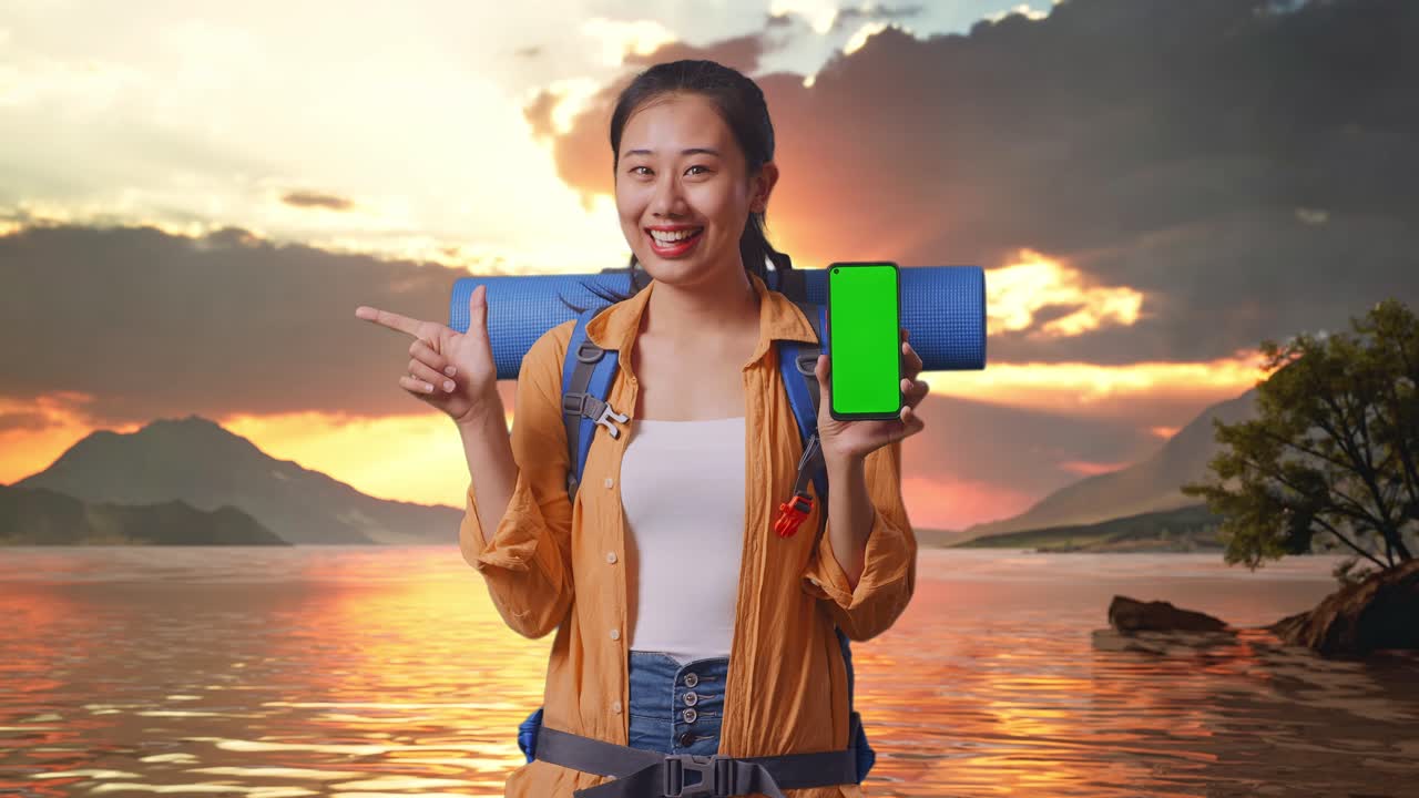 un turista feliz mostrando su teléfono móvil al atardecer junto al lago
