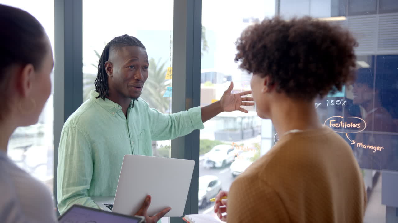 Discussing project, colleagues using laptop and whiteboard in modern office meeting