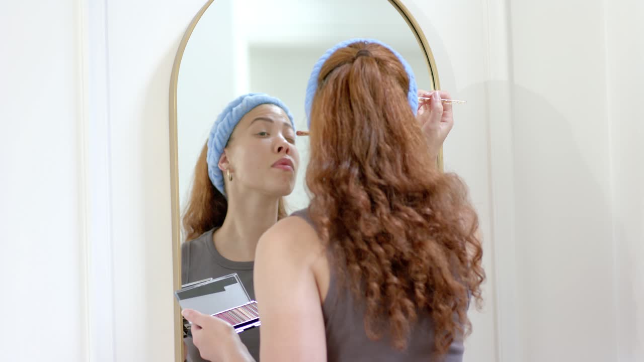 Amiche diverse alla toeletta, mentre un'amica parla con la donna allo specchio che applica l'ombretto, preparandosi.
